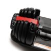 A close-up of an adjustable dumbbell with a black handle and weight plates, featuring a red locking mechanism and a numbered dial for selecting weight increments, resting on a black tray.