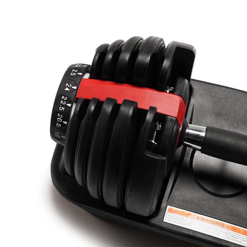 A close-up of an adjustable dumbbell with a black handle and weight plates, featuring a red locking mechanism and a numbered dial for selecting weight increments, resting on a black tray.