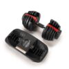 Adjustable dumbbell with multiple weight plates, resting beside its black plastic storage and adjustment tray. The dumbbell features a black and red design with a dial for weight selection.