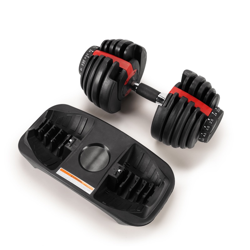 Adjustable dumbbell with multiple weight plates, resting beside its black plastic storage and adjustment tray. The dumbbell features a black and red design with a dial for weight selection.